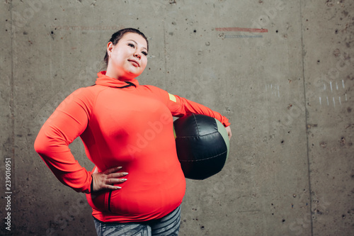 positive plump woman in stylish sportswear holding leather ball and looking at the camera. close up photo. copy space. interest © alfa27