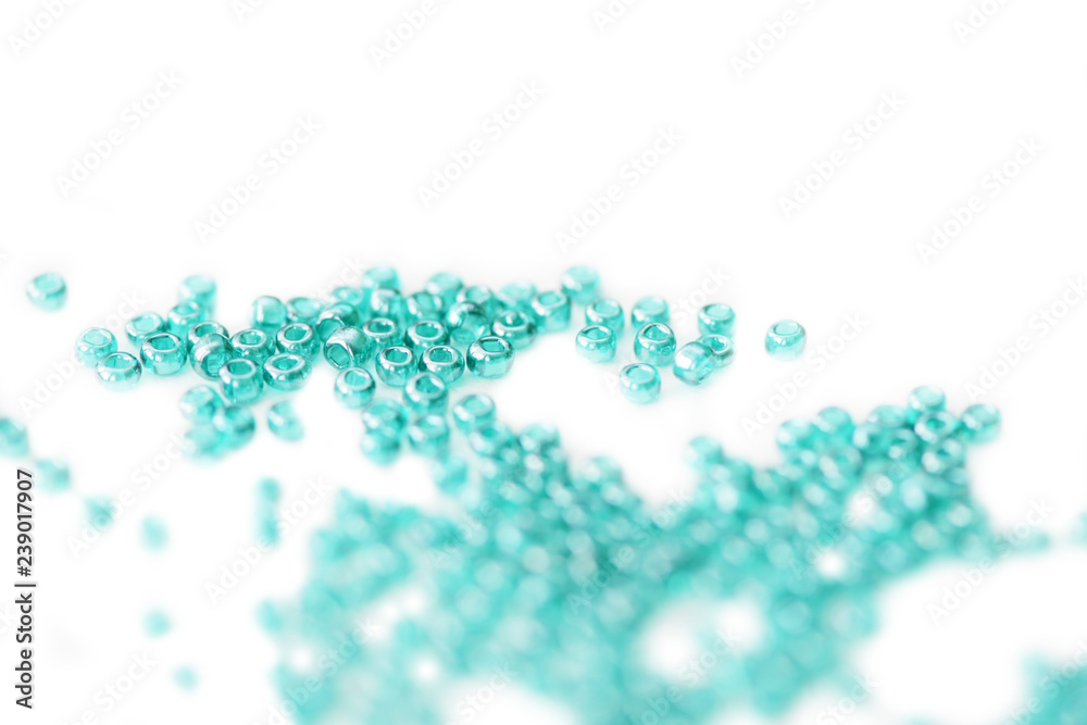 Seed beads of aquamarine color scattered on white surface close up