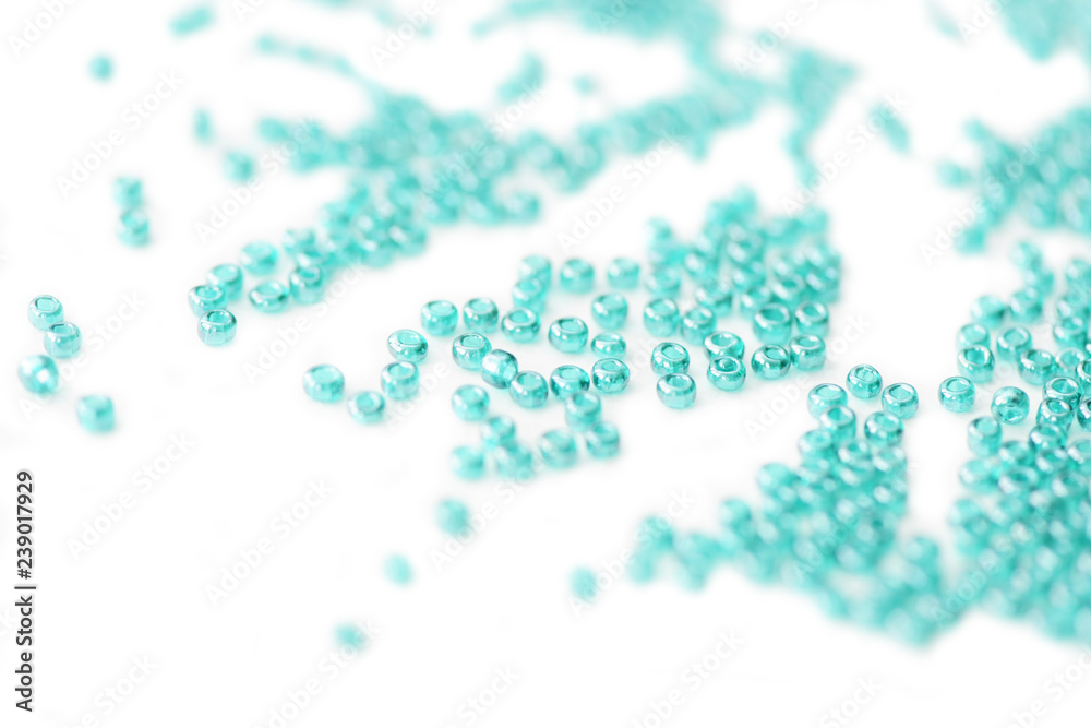 Seed beads of aquamarine color scattered on white surface close up