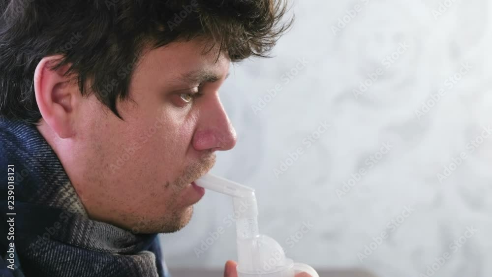 Use nebulizer and inhaler for the treatment. Sick man inhaling through inhaler nozzle for throat. Close-up face side view. Use nebulizer and inhaler for the treatment. Sick man inhaling through inhaler nozzle for throat. Close-up face side view.