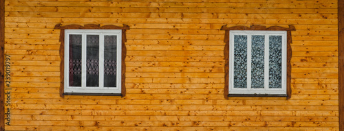 Two white wooden windows in the wall of raw brown wooden boards with knots. Frontal view. Close-up. © somemeans