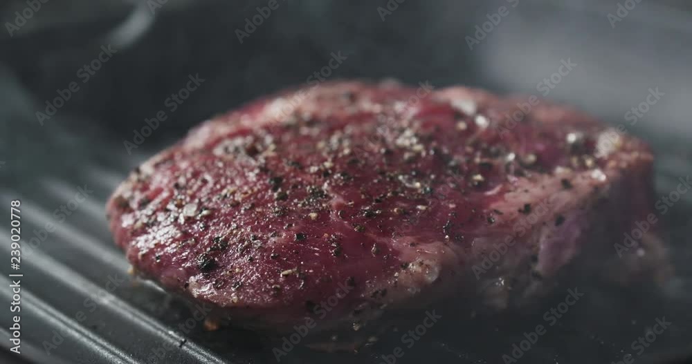 Slide slow motion shot of cooking rib eye steak on grill pan