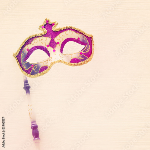 carnival party celebration concept with elegant gold, pink and purple mask on stick over white wooden background. Top view.