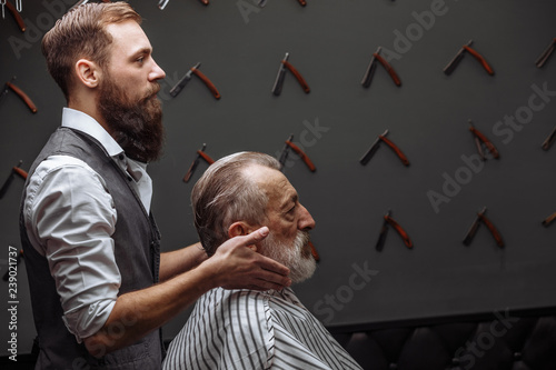 Senior man visiting hairstylist in barber shop. Close up of professional groomed barber trimming senior client grey hair with razor. Man s Beauty Salon, Barbershop Concept.