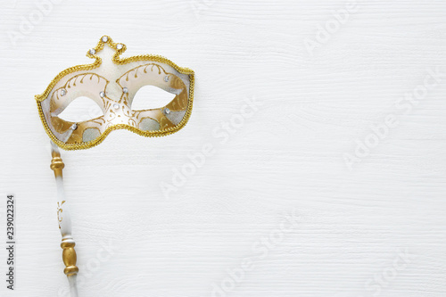 carnival party celebration concept with elegant gold mask on stick over white wooden background. Top view.