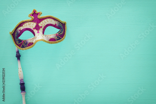 carnival party celebration concept with elegant purple mask on stick over mint wooden background. Top view.