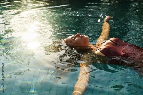 Bild auf Leinwand beautiful female relaxing in an outdoors swimming pool with sun reflactions on w