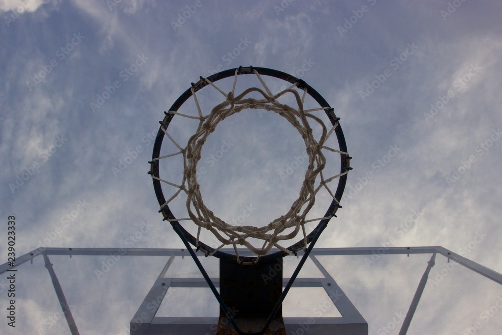Look at the blue cloudy sky trough a basketball ring with net and transparent glass board 