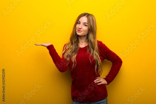Young girl on vibrant yellow background holding copyspace imaginary on the palm to insert an ad