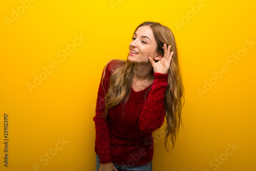 Young girl on vibrant yellow background listening to something by putting hand on the ear