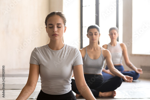 Group training of deep meditation at yoga studio class. Diverse young females sitting with closed eyes in lotus position meditate and visualizing together  feeling self-awareness serenity and calmness