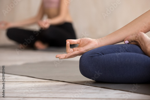 Women during group session meditate sitting in lotus position on yoga mat, close up focus on girl fingers folded in Jnana Mudra. Symbol concept of connection between human and the greater Universe