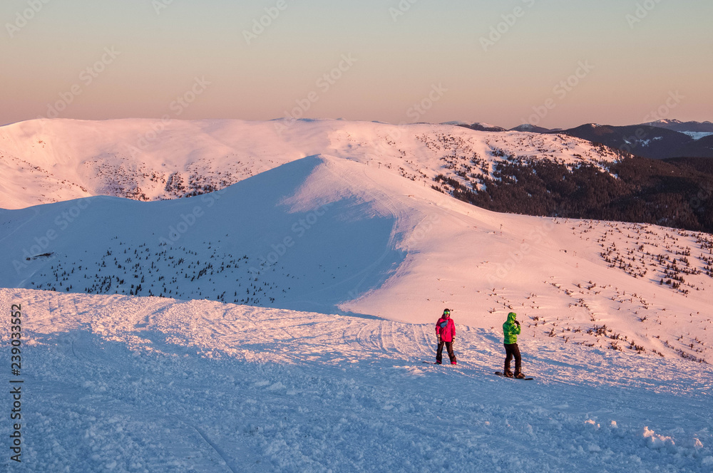 Snowboarders on top of a mountain at sunrise on a frosty winter morning. Snowboarders on the top of the mountain in the Carpathians are preparing for the descent and freeride.