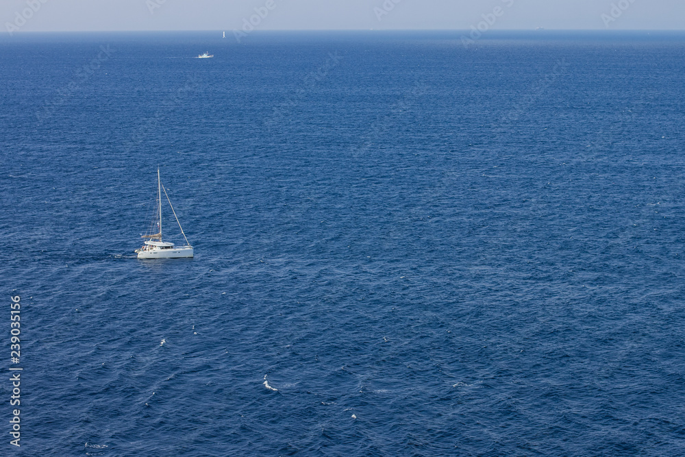 Fototapeta premium small white yacht in Caribbean water surface with horizon line background wallpaper patter with empty space for copy or your text, expensive summer cruise vacation concept