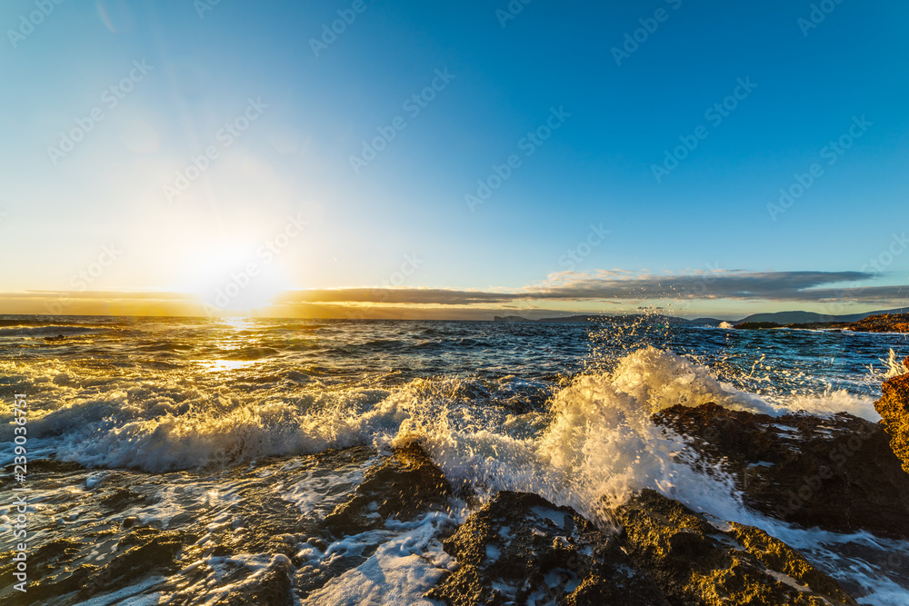 Fototapeta premium Waves crashing against the rocky shore at sunset