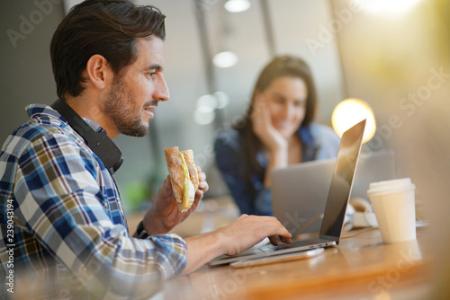 Quadro su tela Attractive man eating sandwich whilst working in co working space