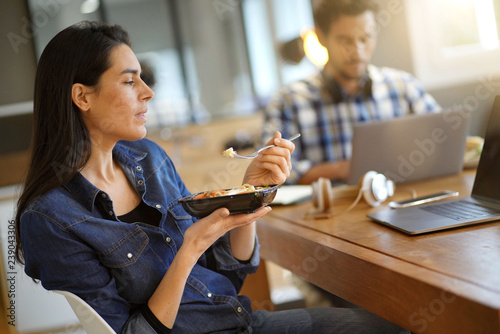 Quadro su tela Beautiful woman eating lunch whilst working in co working space