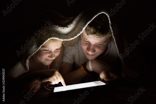 Boy and girl using a tablet at night under a blanket