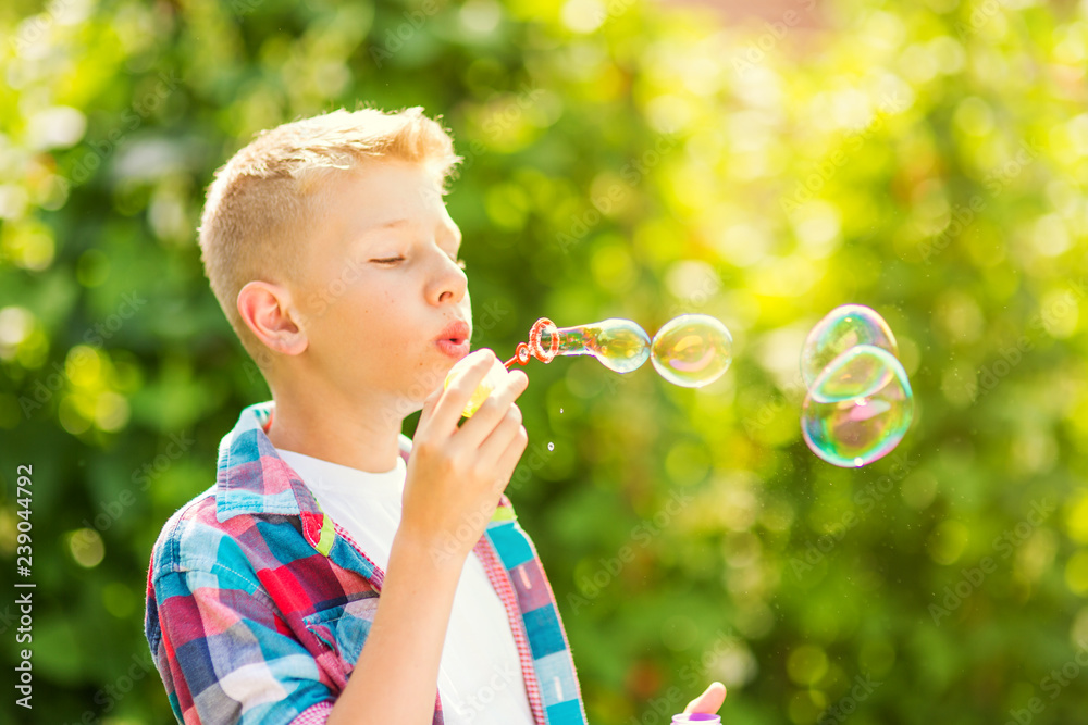 Portrait of a young boy blowing soap bubbles in a park
