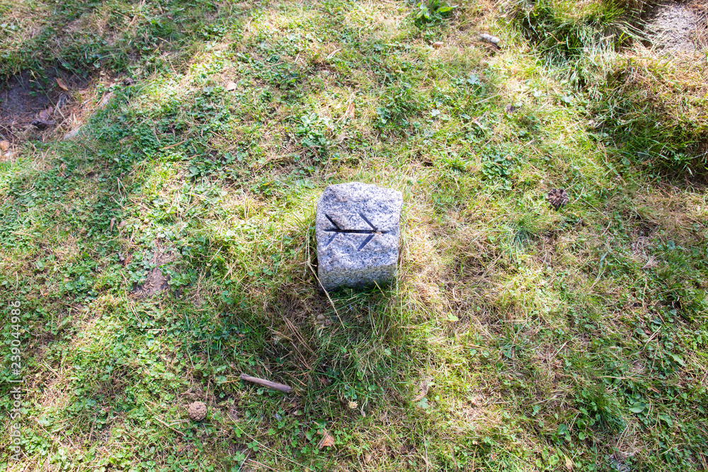 Obraz premium double arrow sculpted on a stone to signal the way or a trail for trekking or rural biking on the green grass of a meadow