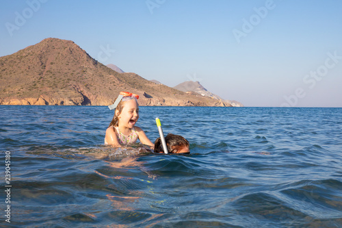happy little girl with diving glasses on back of woman snorkeling in the water of Genoveses Beach, in Cabo de Gata Natural Park (Almeria, Andalusia, Spain) © Q