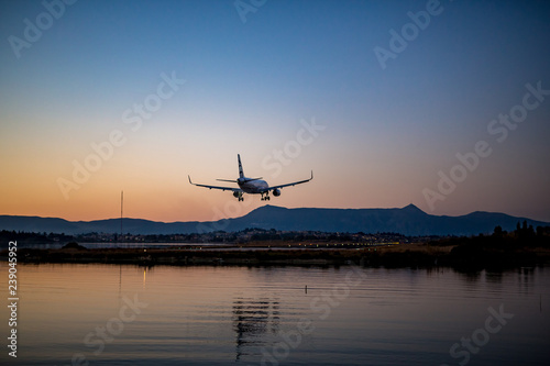 Passenger airplane is landing at Corfu airport at sunset, the golden hour, airport lights are on. Kerkyra Island, Greece, clear sky spring evening