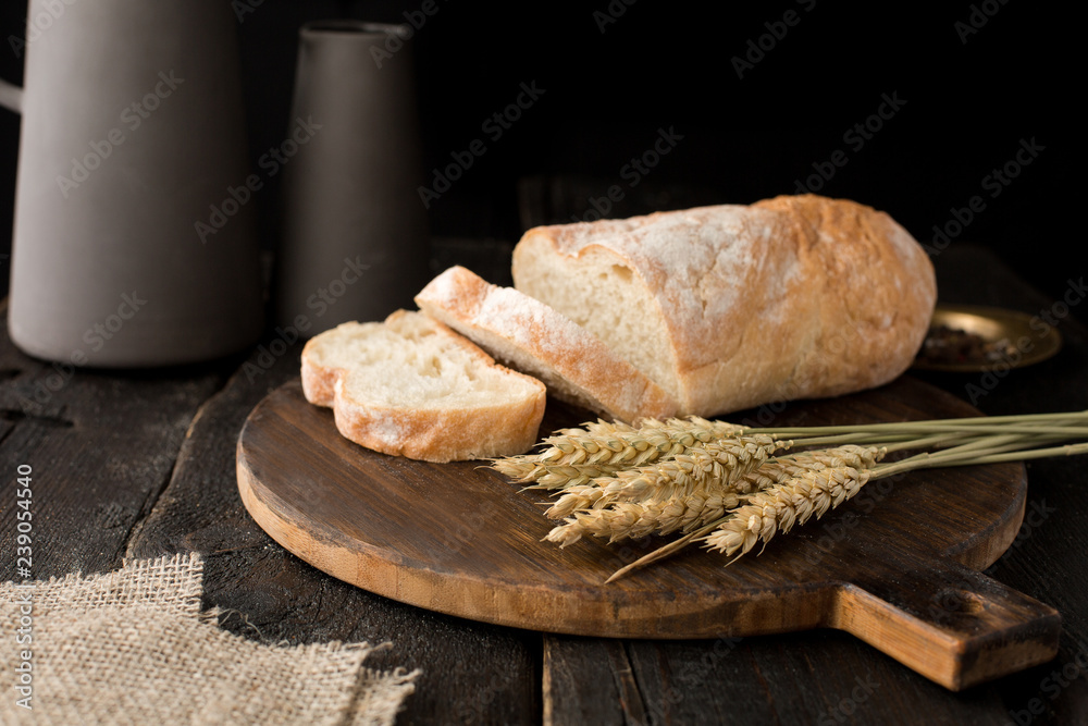 Fresh bread on a board with wheat on a wooden background Fresh bread on a board with wheat on a wooden background
