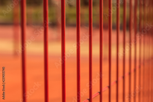 lawn field for playing basketball behind the orange fence mesh. Metal mesh wire fence with tennis court. 