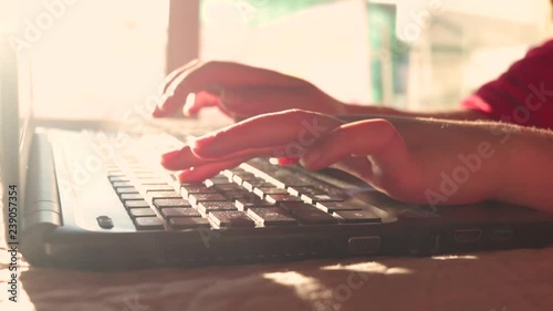 Closeup of hands of a young girl typing on a modern Laptop keyboard. Beautiful highkey  sunrise light. Slow panning