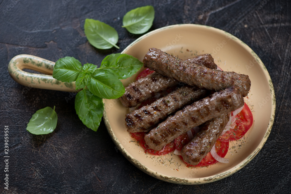 Serving pan with grilled balkan cevapi or skinless beef sausages, studio shot on a dark brown stone background Serving pan with grilled balkan cevapi or skinless beef sausages, studio shot on a dark brown stone background