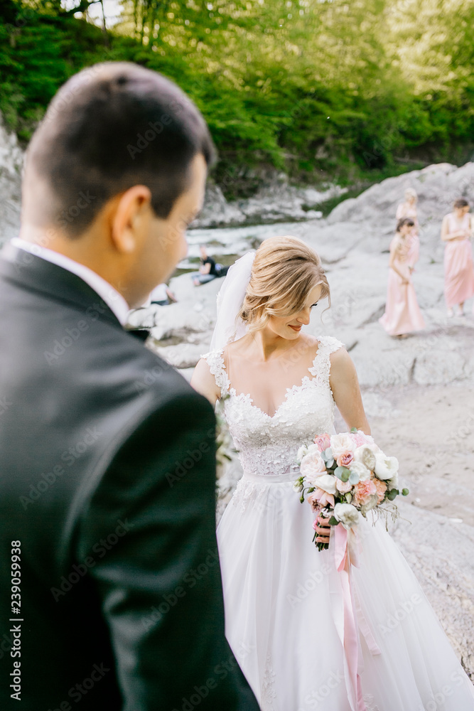 Romantic wedding couple near mountain river. Bride and groom sitting at stone near water. Wedding day. Romantic wedding couple near mountain river. Bride and groom sitting at stone near water. Wedding day.