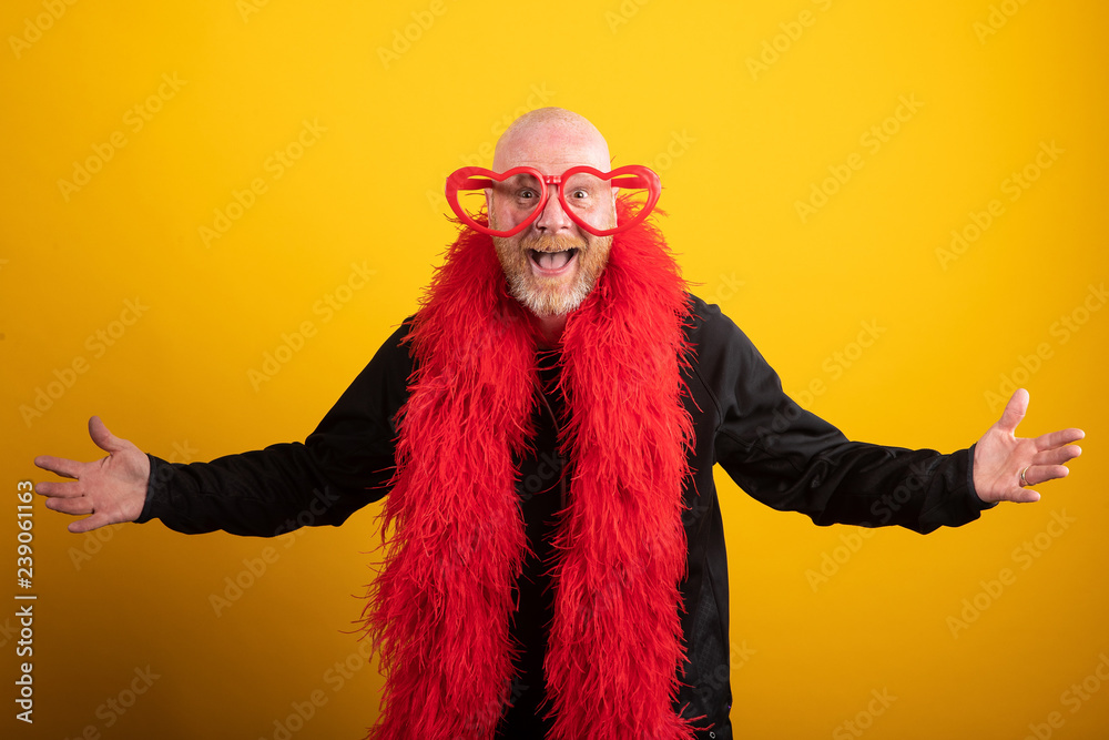 Bald man having fun wearing vibrant red feather boa and heart shaped glasses Bald man having fun wearing vibrant red feather boa and heart shaped glasses