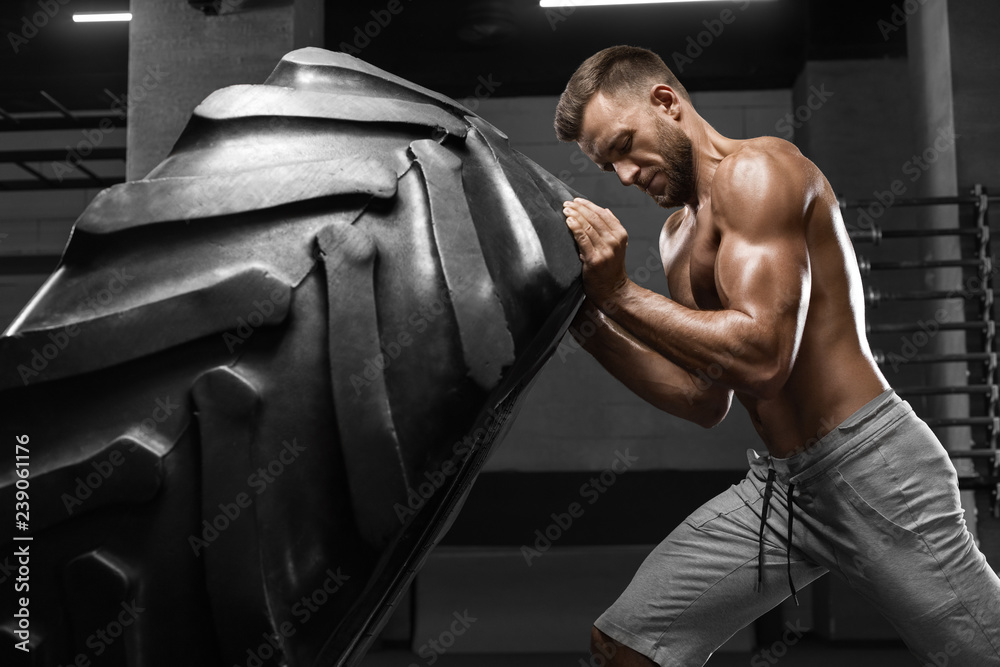 Muscular man working out in gym flipping tire, strong male naked torso abs Muscular man working out in gym flipping tire, strong male naked torso abs