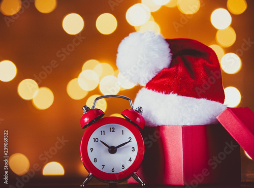 Vintage alarm clock with Santa Claus hat, box and Fairy Lights on background