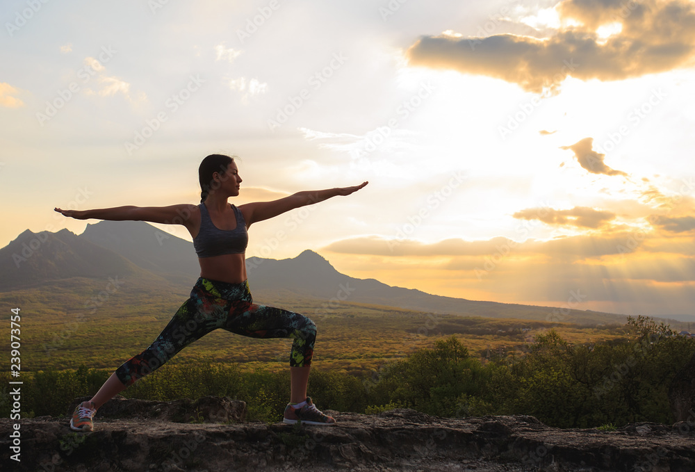 Silhouette of young woman practicing yoga or pilates at sunset or sunrise in beautiful mountain location. Silhouette of young woman practicing yoga or pilates at sunset or sunrise in beautiful mountain location.