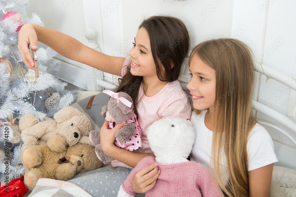 Sharing the images on social media. Happy children with mobile phone. Taking Christmas and New Year selfie with smartphone. Little girls use phone in bed. Merry Christmas and Happy New Year greetings Sharing the images on social media. Happy children with mobile phone. Taking Christmas and New Year selfie with smartphone. Little girls use phone in bed. Merry Christmas and Happy New Year greetings