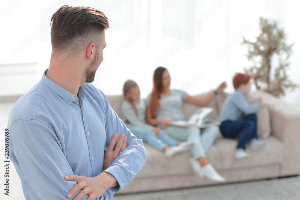 Fototapeta premium man standing in his living room and looking at his family