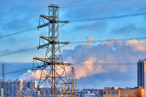 Supports of high-voltage power lines, modern houses, roads, Smoking pipes. In the foreground are trees without leaves, shrubs, and withered, autumn grass.
