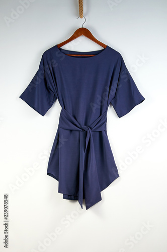 Unusual stylish dress on a hanger on a white background isolated isolate. Short navy blue dress with a wide belt. Original idea of demonstrating a dress on a hanger for a blog, advertising, magazine.