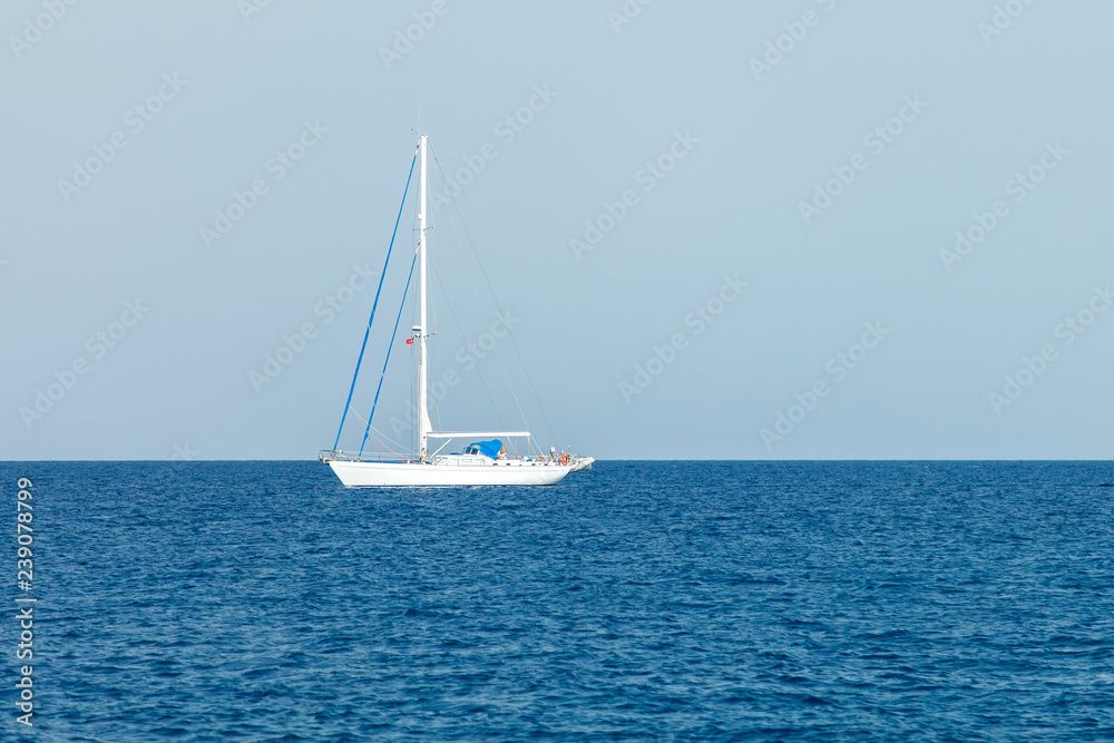 A lone white yacht with lowered sails stands in the waters of the Mediterranean Sea
