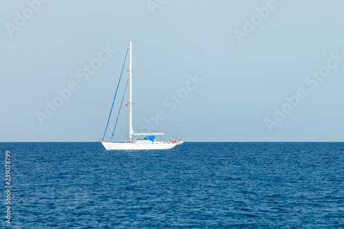 A lone white yacht with lowered sails stands in the waters of the Mediterranean Sea