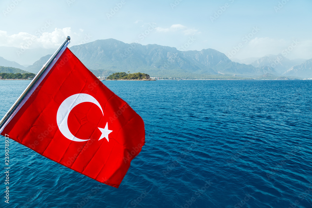 Fototapeta premium Turkish flag flying in the wind against the background of the sea and the coast