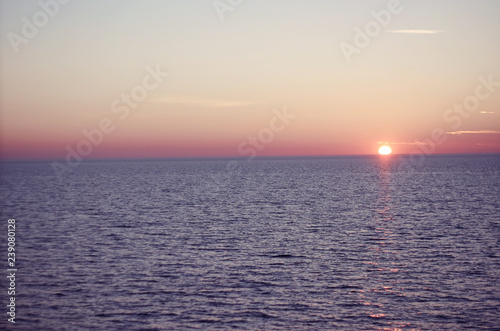 Early in the morning the sun rises above the water surface against the clear sky
