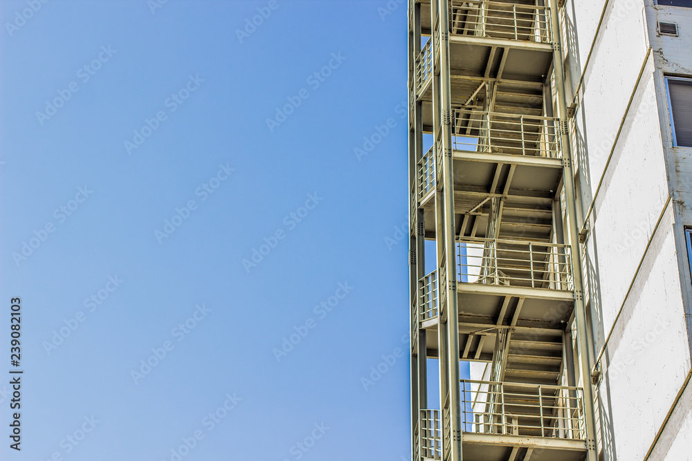 Fototapeta premium metal fire escape stairs construction outdoor side of high building and empty blue sky, copy space