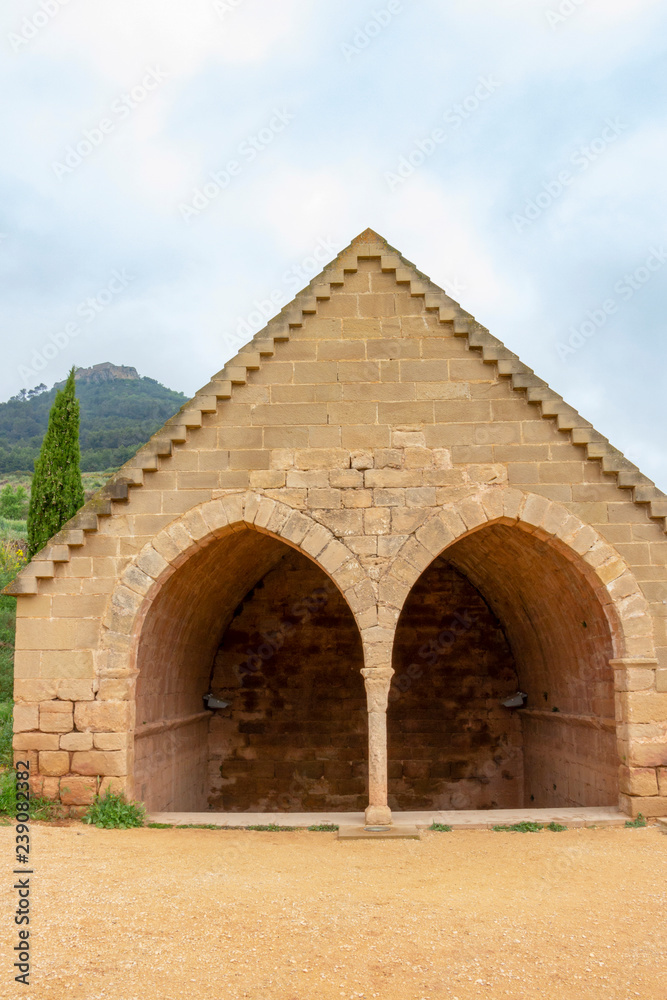 The double arched building of Fuenta de los Moros, the Gothic Fountain of the Moors, the ruins of Castillo de Monjardin in the background, at Villamayor de Monjardin Spain