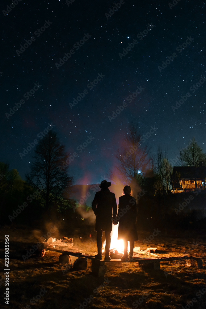 Couple in love around the campfire at night. Starry Sky. Nature lovers are standing around a campfire at night.