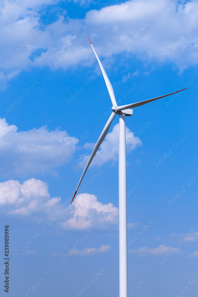 One single windmill turbine with partly cloudy blue sky in background. Renewable energy wind turbine