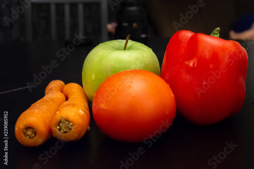 Carrots, tomoto and apple placed on black dining table photo