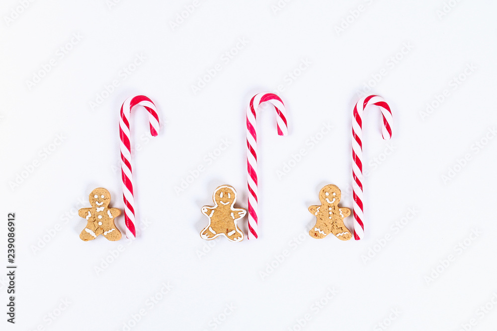 Obraz premium Christmas layout. Striped red-white cane candies and homemade ginger cookies on a white background. New Year 2019, christmas, winter concept. Copy space, tov view, flat lay composition.