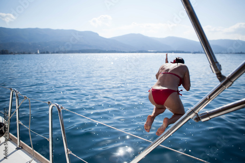 Summer in Greece. Funny woman wearing red swimsuit is jumping into the sea, sun, boat and fun © vetakrivosheeva